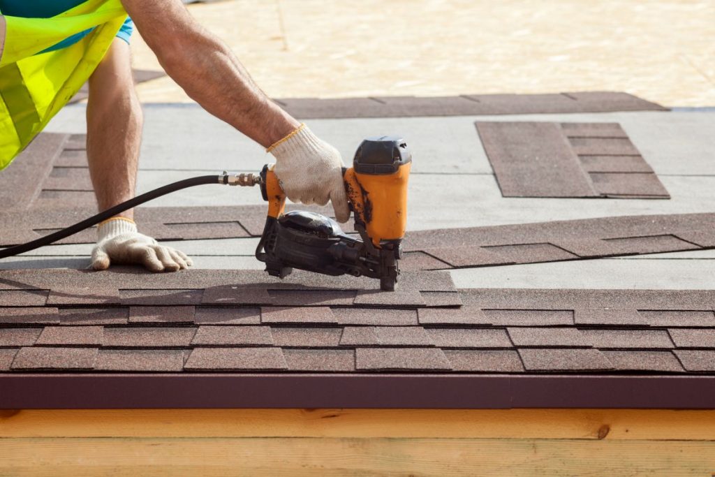 Construction worker putting the asphalt roofing (shingles) with nail gun on a new frame house, Lakeville